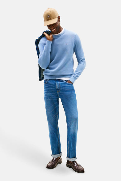 Blauwe trui met ronde hals van Tommy Hilfiger, met een denim jas over de schouder, gedragen met jeans en bruine loafers.