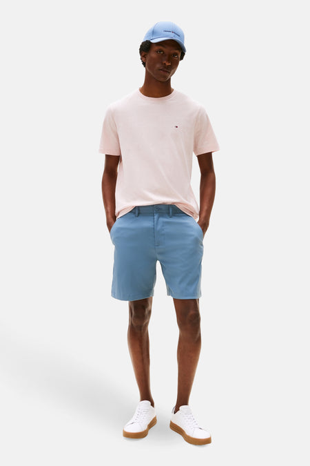 T-shirt rose à manches courtes de TOMMY HILFIGER, porté avec des shorts bleus et des baskets blanches.