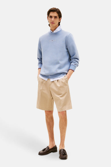 Blauwe sweater van Tommy Hilfiger, gedragen met een overhemd en gestreepte shorts met bruine loafers.
