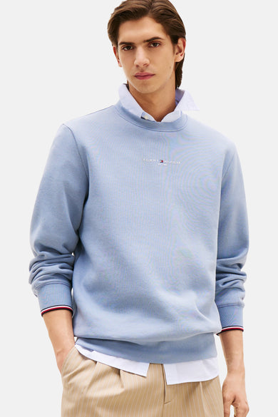 Blauwe sweater van TOMMY HILFIGER, gedragen met een wit overhemd en gestreepte broek.