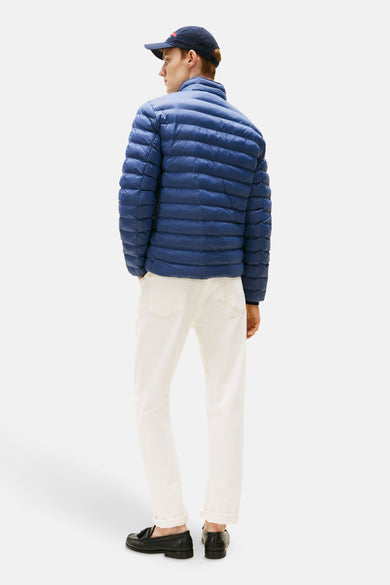 Courte veste bleue de TOMMY HILFIGER, avec des coutures horizontales, associée à des jeans blancs et des loafers noirs.