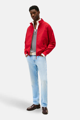 Rechte lichtblauwe denim jeans van Tommy Hilfiger, gecombineerd met een gestreepte trui, rood jack en bruine loafers.
