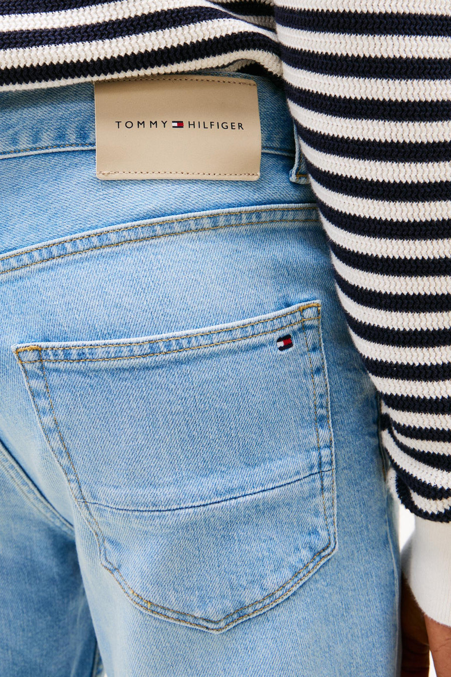 Jean droit en denim bleu clair de Tommy Hilfiger, avec poche arrière et pull rayé sur le côté, court.