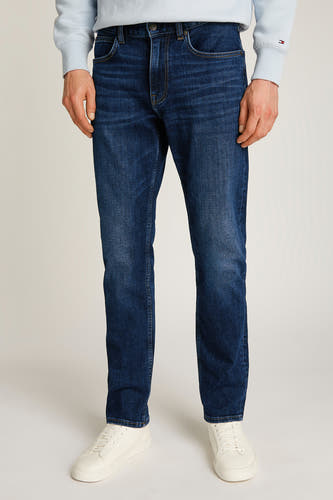 Jeans straight model in donkerblauw denim van TOMMY HILFIGER, gedragen met witte sneakers en een lichtblauwe trui.
