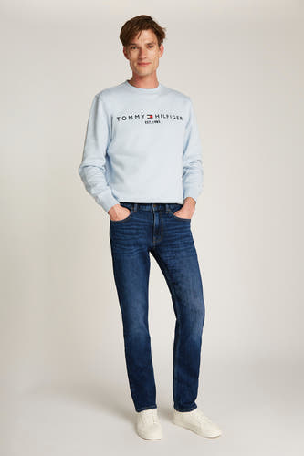Rechte donkerblauwe denim jeans van Tommy Hilfiger, gedragen met een lichtblauwe trui en witte sneakers.