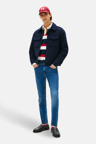 Slim fit jeans van TOMMY HILFIGER, met een middenblauwe denim wassing, gecombineerd met een rugby shirt, jas en loafers.
