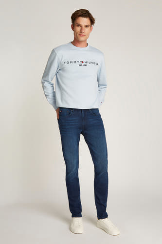Rechte donkerblauwe denim jeans van Tommy Hilfiger, gedragen met een lichtblauw sweatshirt en witte sneakers.
