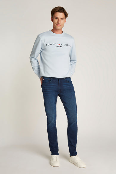 Rechte donkerblauwe denim jeans van Tommy Hilfiger, gedragen met een lichtblauw sweatshirt en witte sneakers.
