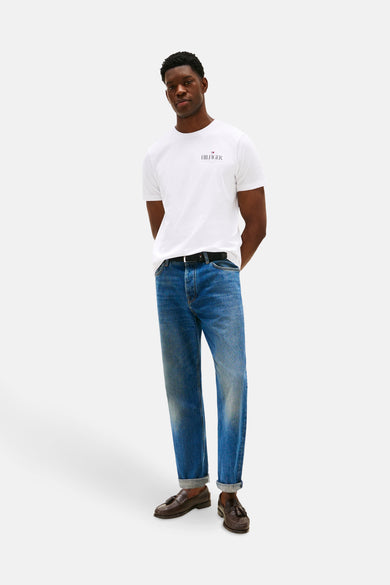 Wit T-shirt met korte mouwen van TOMMY HILFIGER, gedragen met blauwe jeans, een zwarte riem en bruine loafers.