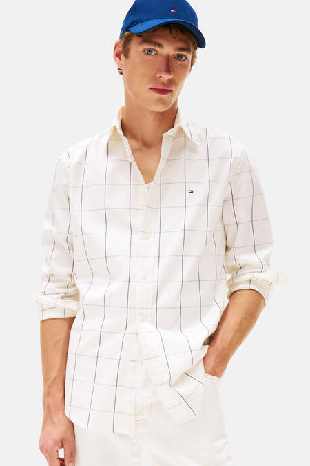 Chemise beige à manches longues de TOMMY HILFIGER, avec un motif à carreaux noirs, associée à des pantalons blancs et une casquette bleue.