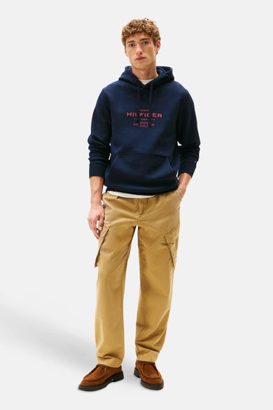 Blauwe sweater met kap van Tommy Hilfiger, gedragen met een wit T-shirt en kaki cargo broek, met bruine schoenen.
