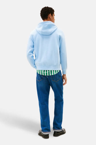Blauwe sweater met kap van Tommy Hilfiger, met een gestreept shirt eronder en spijkerbroek.