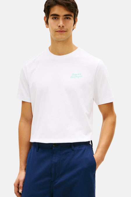 Wit T-shirt met korte mouwen van Tommy Hilfiger, voorzien van een lichtgroen geborduurd scriptlogo op de borst, gedragen met een donkerblauwe broek.