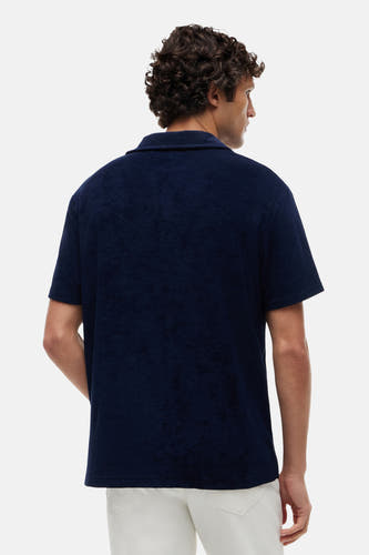 Polo en éponge bleu de TOMMY HILFIGER à manches courtes, vue de dos d'un homme en pantalon blanc.