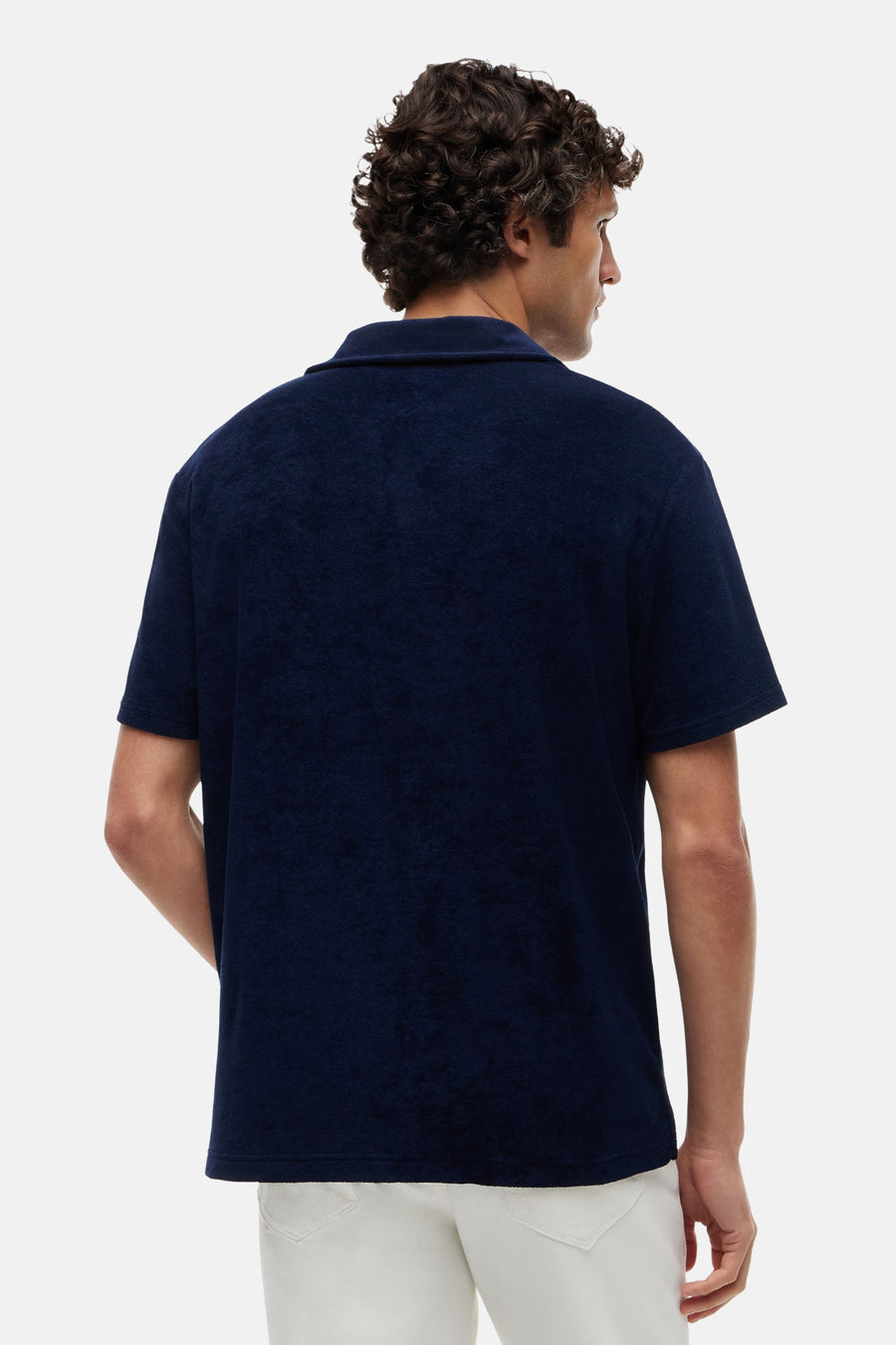 Polo en éponge bleu de TOMMY HILFIGER à manches courtes, vue de dos d'un homme en pantalon blanc.