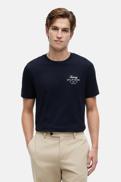 T-shirt bleu marine de TOMMY HILFIGER avec logo sur la poitrine, porté par un homme avec un pantalon beige.