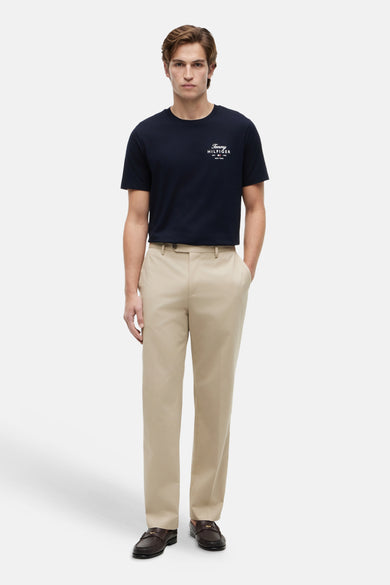 T-shirt bleu TOMMY HILFIGER avec logo et texte blancs sur la poitrine, porté par un homme avec un pantalon beige et des mocassins marron foncé.