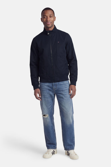 Donkerblauwe korte jas van TOMMY HILFIGER, met rits, opstaande kraag en klein logo op borst, gedragen met lichtblauwe jeans en witte sneakers, front view.
