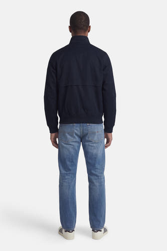 Donkerblauwe korte jas van TOMMY HILFIGER, achterzijde, met ritsdetails en ribboorden, gedragen met blauwe jeans en witte sneakers.