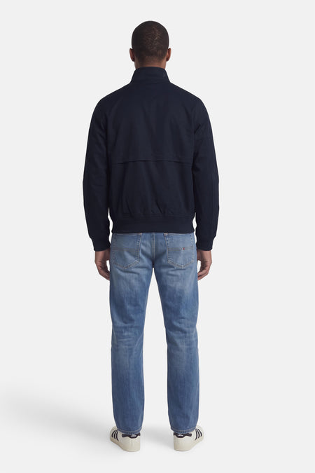 Donkerblauwe korte jas van TOMMY HILFIGER, achterzijde, met ritsdetails en ribboorden, gedragen met blauwe jeans en witte sneakers.