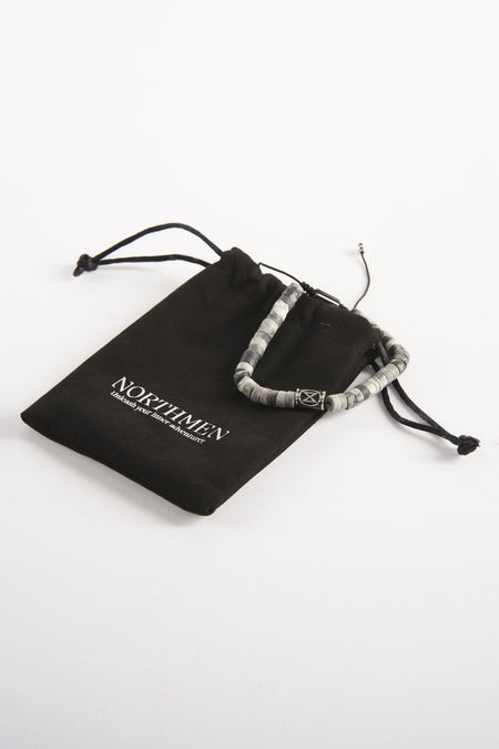 Grijze armband van NORTHMEN, naast een zwarte stoffen zak met trekkoord, op een witte achtergrond.
