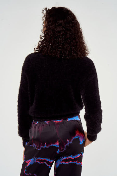 Pull-over noir de NOOR BY NORA GHARIB, en une douce texture et des manches longues, associé à un pantalon avec un imprimé abstrait.