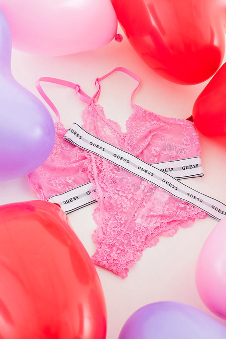 Roze slip van Guess, met kanten details en omringd door rode en paarse ballonnen.

