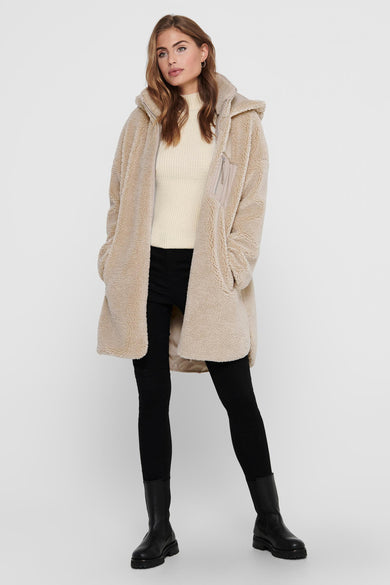 Beige lange jas van ONLY, met capuchon en zwarte broek en laarzen.
