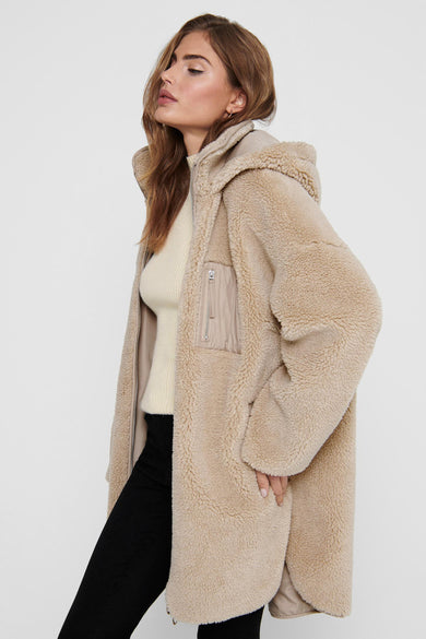 Beige lange jas van ONLY, met capuchon en zwarte broek.