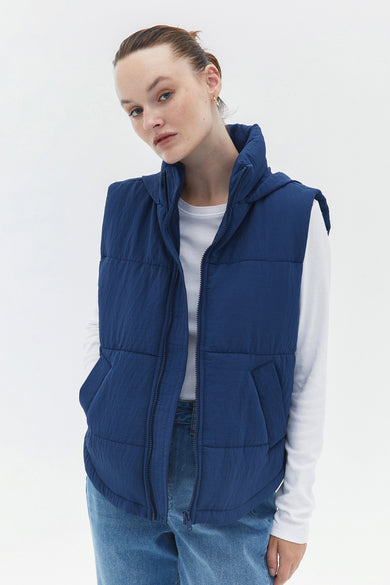 Gilet bleu d'OXXO, avec un longsleeve blanc et des jeans bleus.