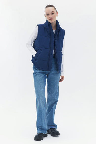 Gilet bleu d'OXXO, avec des coutures verticales, porté sur un t-shirt blanc et des jeans larges.