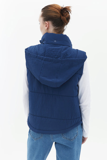 Gilet bleu d'OXXO, avec capuche et jeans visibles ainsi chemise blanche à l'arrière.