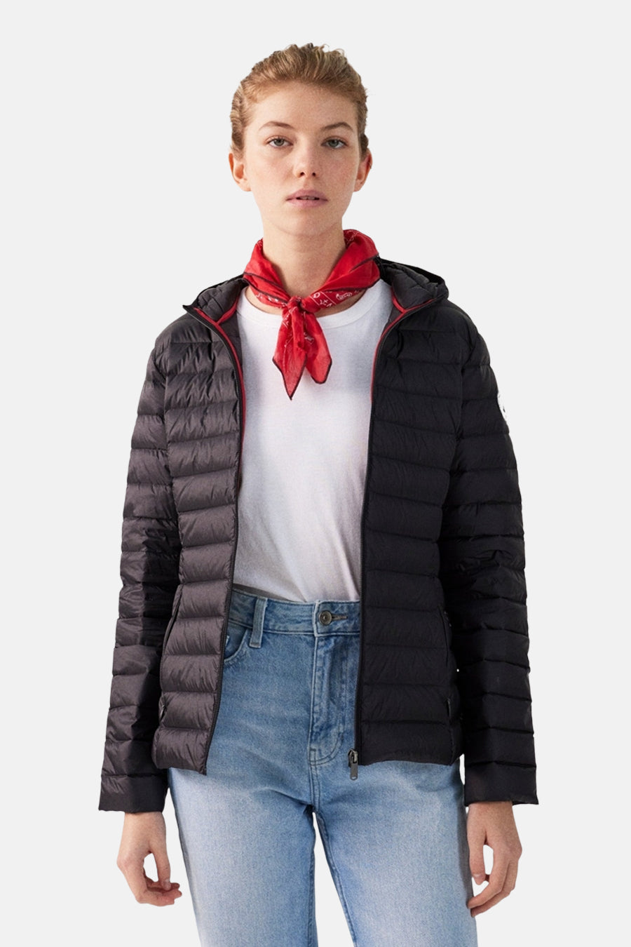Vrouw draagt zwarte donsjas, wit T-shirt en blauwe jeans met een rode bandana om de nek.