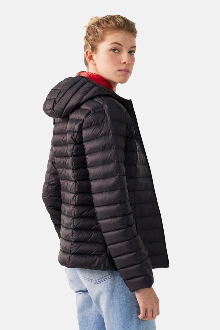 Vrouw met zwarte gewatteerde jas met capuchon en blauwe spijkerbroek.