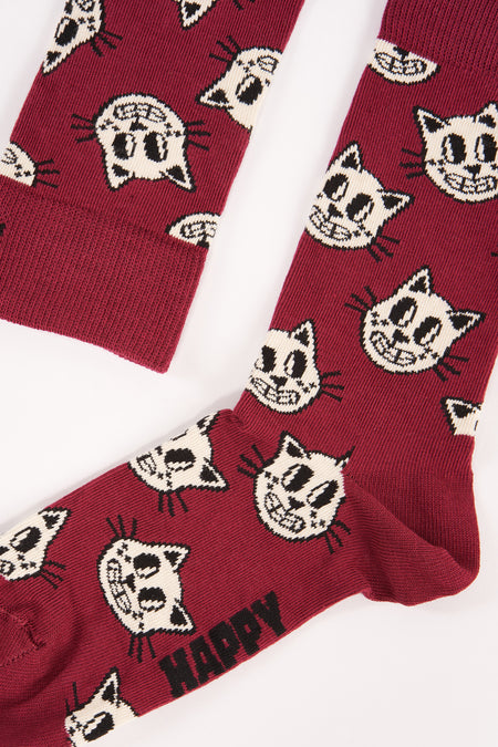 Donkere rode sokken met witte katjesprint van Happy Socks, gestreept en met "HAPPY" tekst aan de zool, platgelegd op wit.