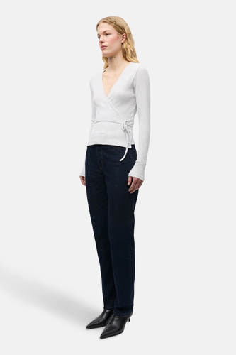 Grijs T-shirt met lange mouwen van ENVII, met overslag en striksluiting, gecombineerd met donkerblauwe jeans en zwarte hakken.
