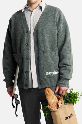 Gilet gris d'ANOTHER COTTON LAB, avec des boutons, des poches et du texte blanc sur l'encadrement, associé à une chemise rayée.