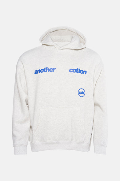 Grijze sweater met kap van ANOTHER COTTON LAB, met blauwe tekst op de borst en een buidelzak aan de voorkant.