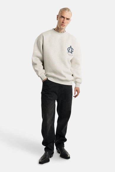 Grijze sweater van ANOTHER COTTON LAB, met een klein marineblauw logo op de borst, gedragen met zwarte jeans en westernlaarzen.
