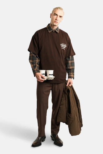 Bruin T-shirt met korte mouwen van ANOTHER COTTON LAB, gedragen over een geruit overhemd, met koffie in de hand.