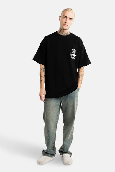 T-shirt noir à manches courtes d'ANOTHER COTTON LAB, avec une impression sur la poitrine, porté avec un jean et des mocassins blancs.