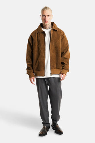 Manteau court brun d'ANOTHER COTTON LAB, avec fermeture éclair et texture corduroy brun, porté avec un T-shirt blanc et un pantalon gris.