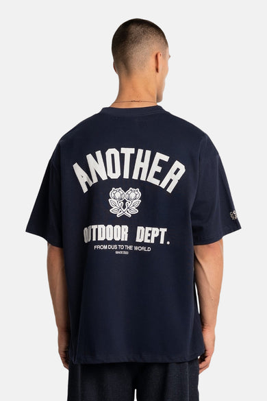T-shirt bleu à manches courtes de ANOTHER COTTON LAB, avec texte blanc et un emblème floral dans le dos.