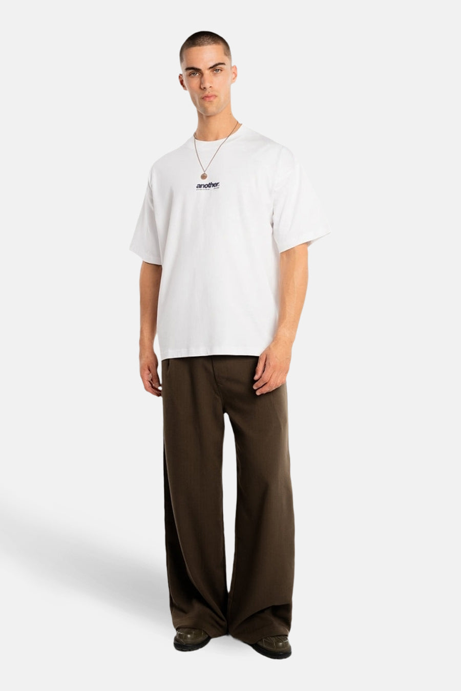 T-shirt blanc à manches courtes de ANOTHER COTTON LAB, porté avec une chaîne dorée et un pantalon marron ample.