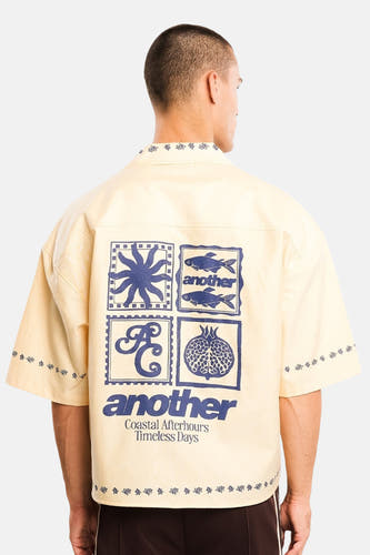 Geel katoenen overhemd met korte mouwen van ANOTHER COTTON LAB, rugzijde met blauwe grafische print en bloemenmotief aan kraag en mouwen, model in lifestyle shot