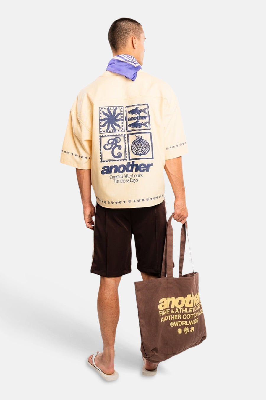 Geel korte mouwen overhemd van ANOTHER COTTON LAB, achterzijde met grafisch print, model draagt donkere korte broek en bruine tas