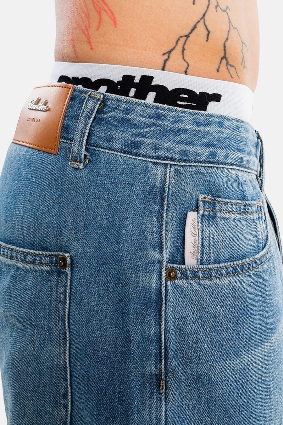 Lichtblauwe denim jeansshort met bruin leerlabel van ANOTHER COTTON LAB, detail van achterzak en taille, close-up.