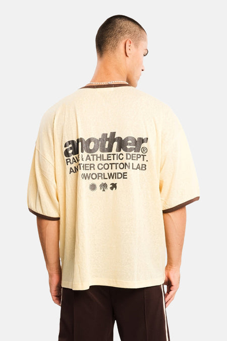 Gele korte mouw t-shirt van ANOTHER COTTON LAB, achterkant met zwart logo en palmboomprint, model in lifestyle pose