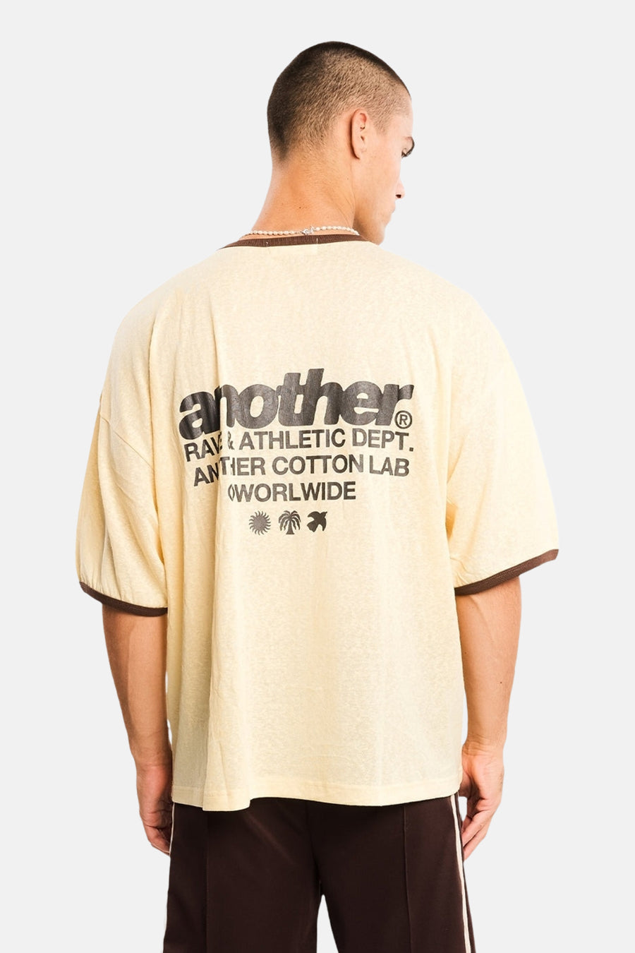 Gele korte mouw t-shirt van ANOTHER COTTON LAB, achterkant met zwart logo en palmboomprint, model in lifestyle pose