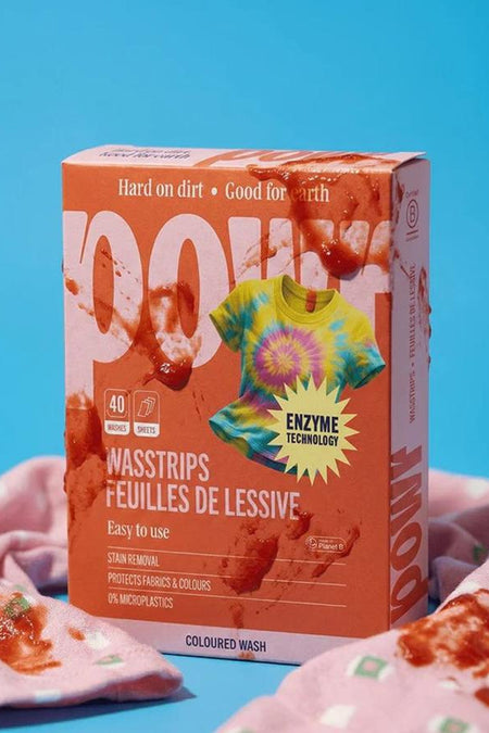 Oranje wasstripsverpakking van WONDR CARE met tie-dye shirt, rode vlekken en roze wasdoeken, front view